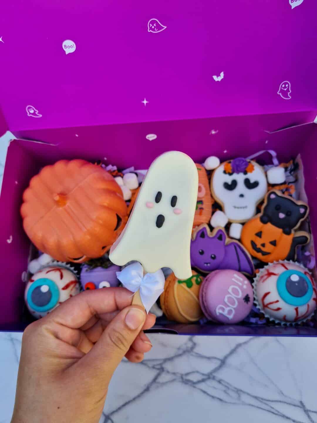 Muñeco de galleta con forma de fantasma en caja de Halloween con decoraciones temáticas.