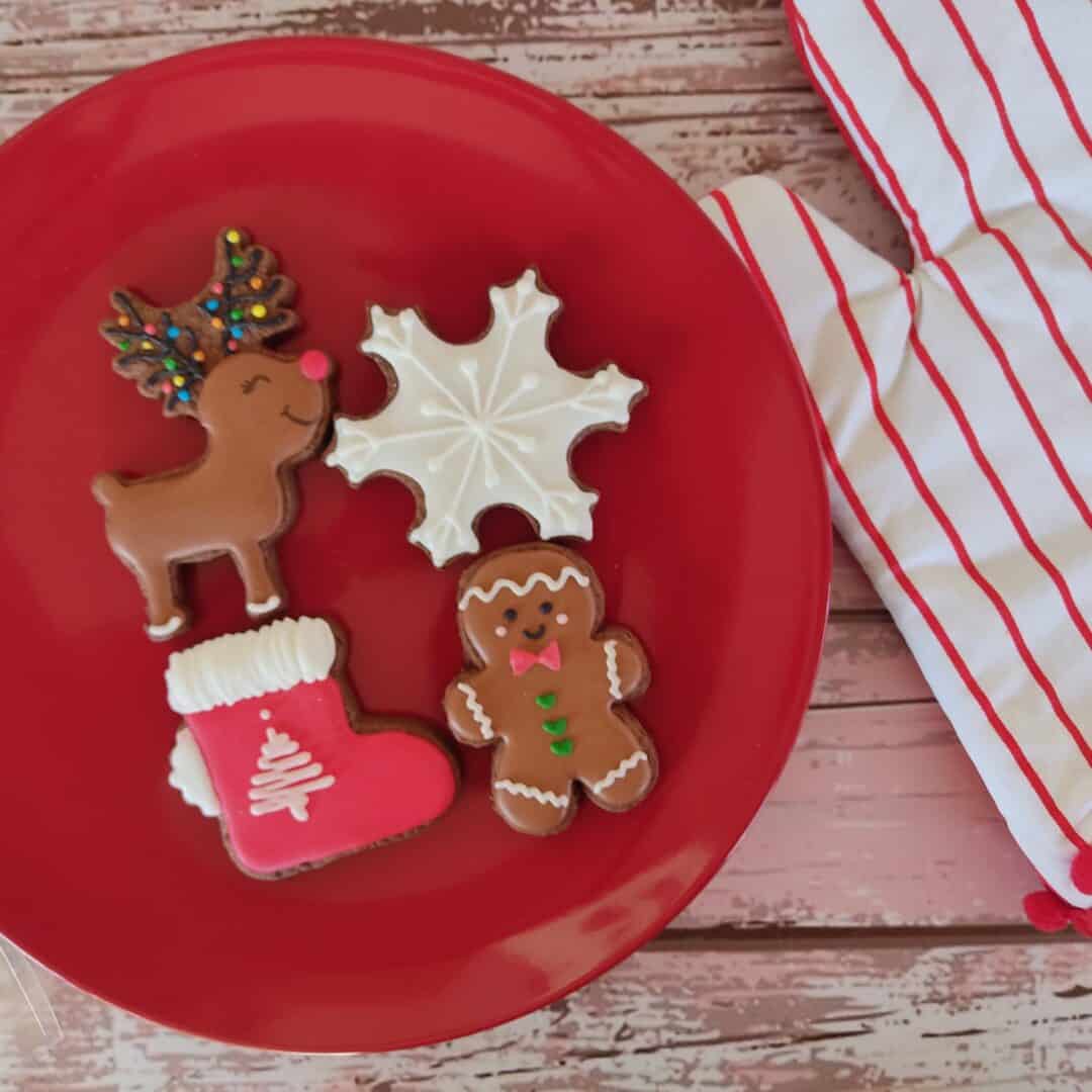 Árbol de Navidad de galleta de jengibre decorada con glaseado y confites, junto a una galleta de muñ.