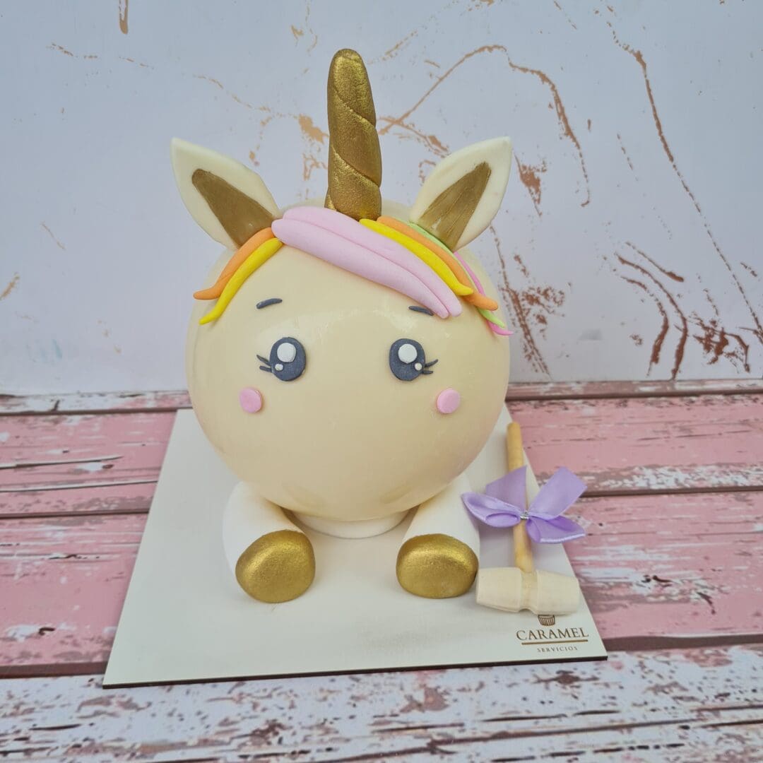 Mordisco de pastel de unicornio con cuerno dorado y lazo en patas delanteras.