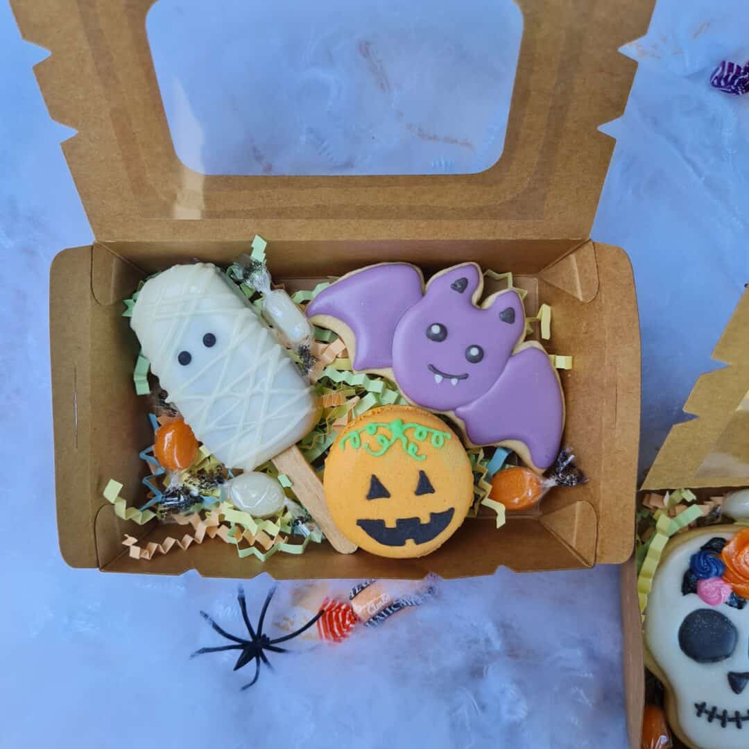 Galletas decoradas de Halloween en caja con fantasmas, calabaza y murciélago.