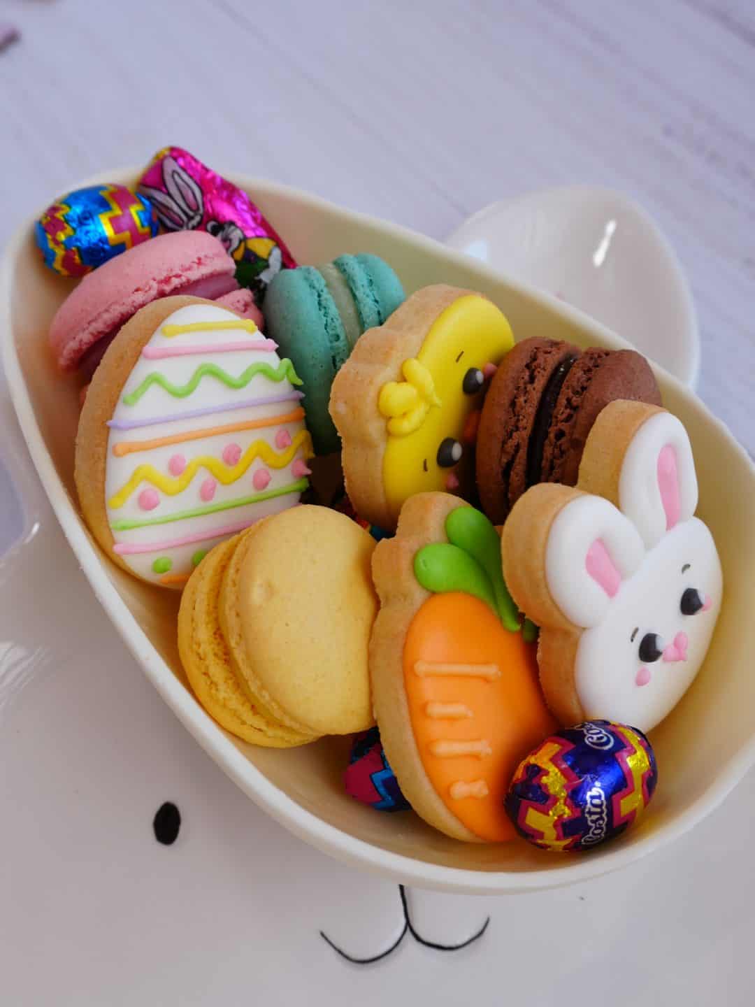 Dulces decorados en forma de huevos, conejitos y zanahorias para Pascua en una bandeja blanca.